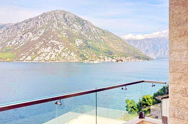 Karadağ, Morinj’deki konut kompleksinin balkonundan Kotor Körfezi ve dağların panoramik manzarası, cam korkulukla birlikte.