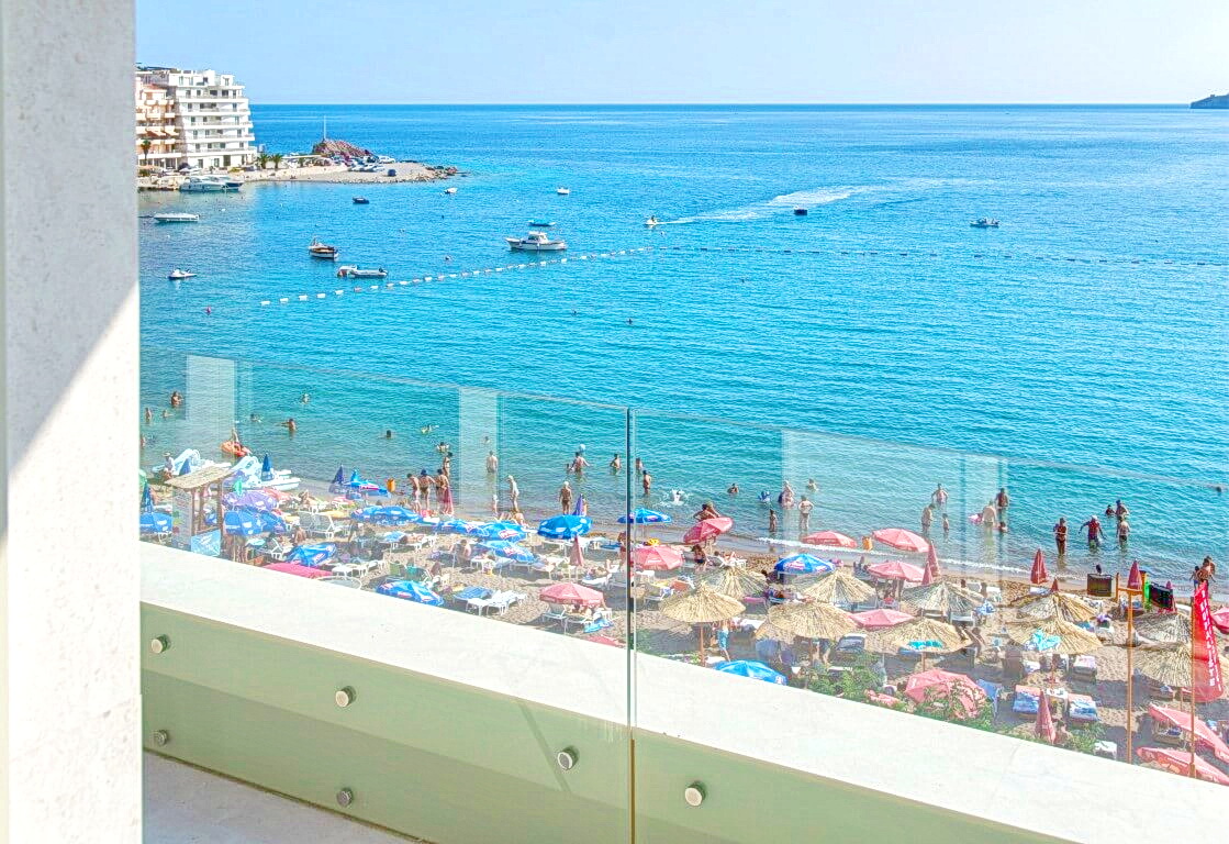 Karadağ, Rafailovići’deki dairenin balkonundan görünüm: cam korkuluk üzerinden plaj, deniz ve yatların panoraması.
