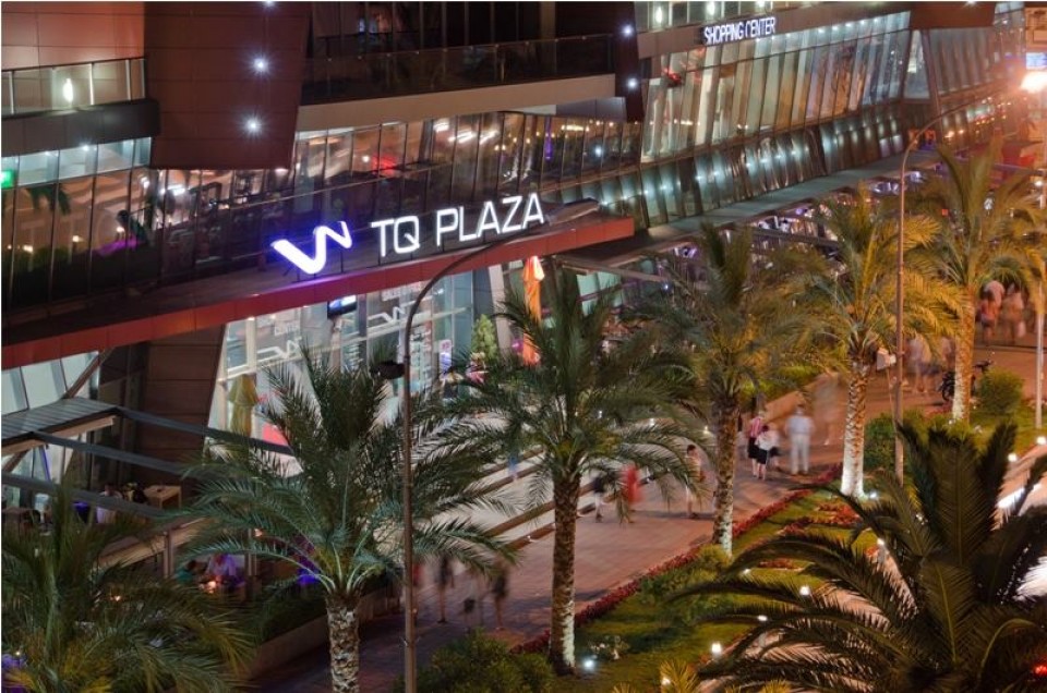 Abendansicht des Einkaufszentrums TQ Plaza im Stadtzentrum von Budva, Montenegro, mit Palmen und moderner Beleuchtung.