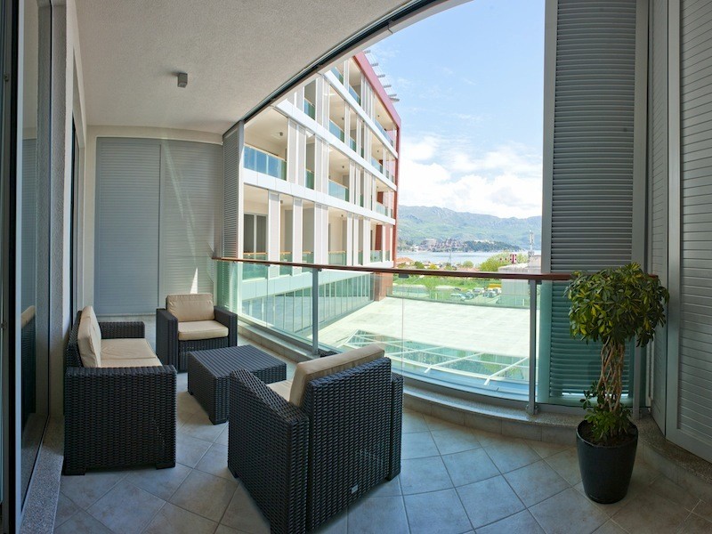 Terrasse mit geflochtenen Möbeln in einer Wohnanlage in Budva, Montenegro, mit Blick auf das Meer und die Berge.