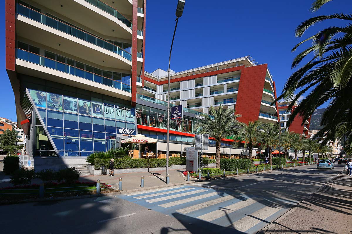 Moderner Wohnkomplex mit Gewerbeflächen in Budva, Montenegro: Blick auf die Fassade des Gebäudes und die Straße.
