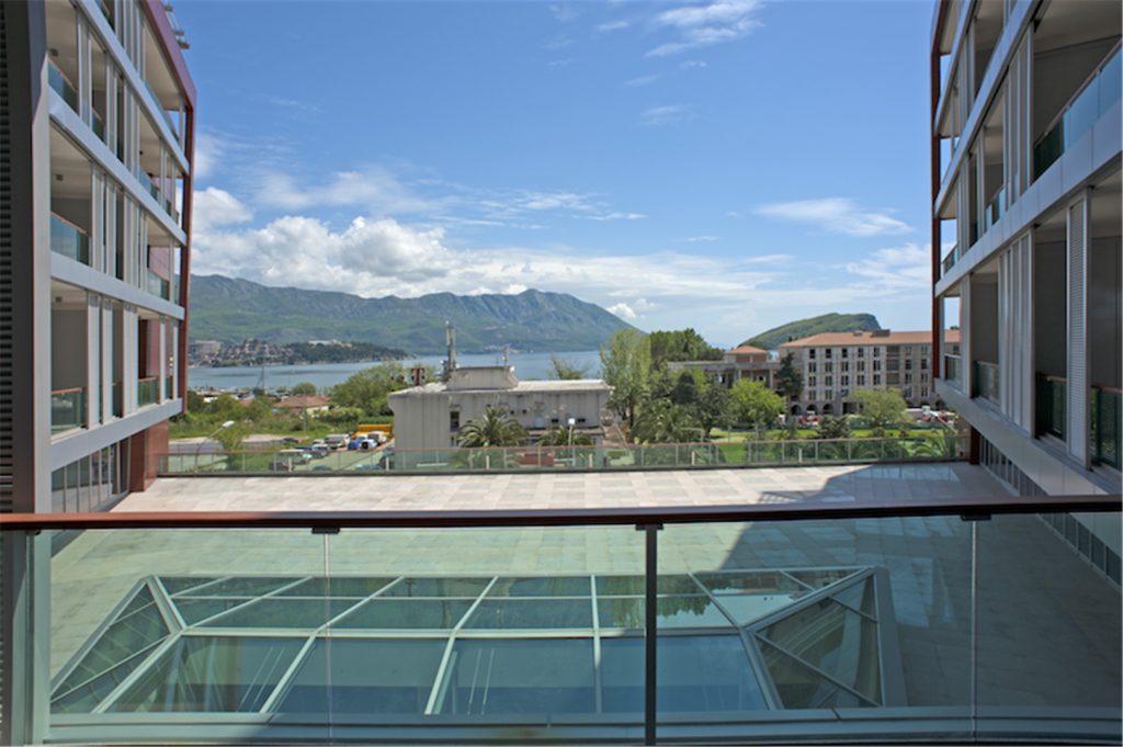 Blick vom Balkon eines modernen Wohnkomplexes in Budva, Montenegro: Panorama von Meer, Bergen und dem Glasdach des Gebäudes.