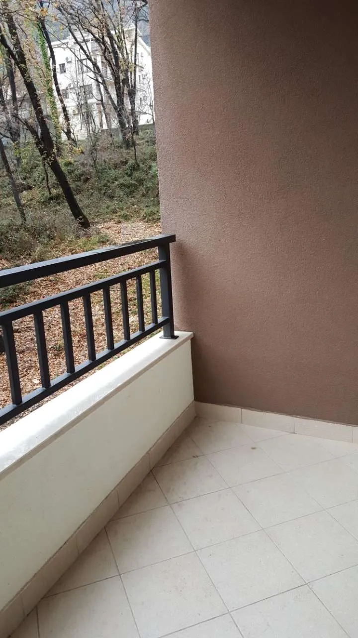 Ein kleiner Balkon mit Metallgeländer, Fliesenboden und Blick auf Bäume und ein Gebäude.