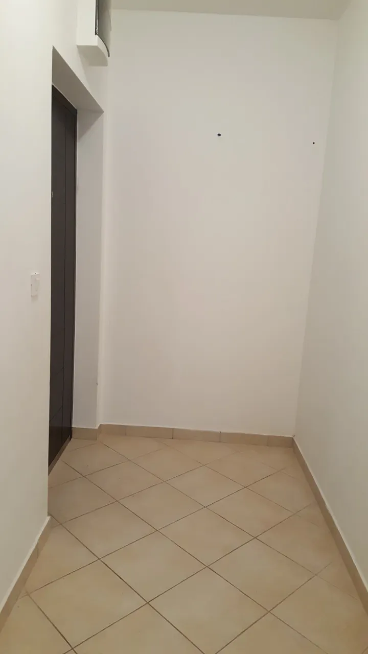 Blick auf einen hellen, leeren Flur mit Fliesenboden und einer dunklen Tür.