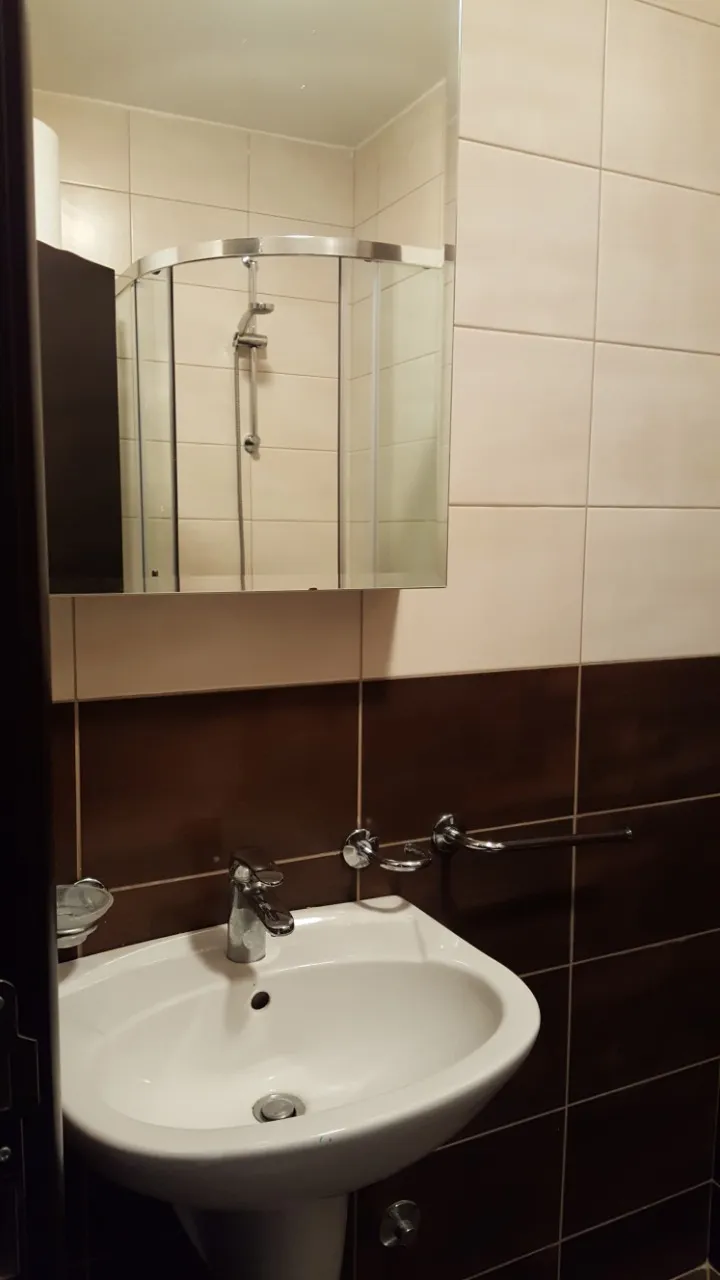 Ein kompaktes weißes Waschbecken mit Chromarmatur an einer braun gefliesten Wand unter einem Spiegelschrank.