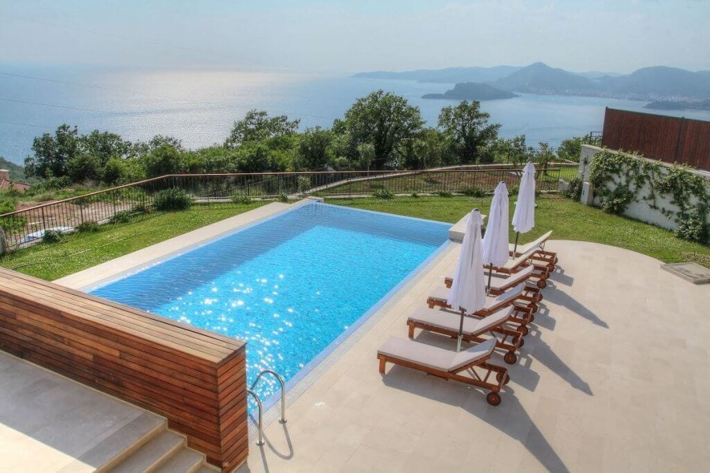 Bazen sa panoramskim pogledom na more kod vile u Blizikućama, Crna Gora: ležaljke, suncobrani i terasa obložena kamenom.