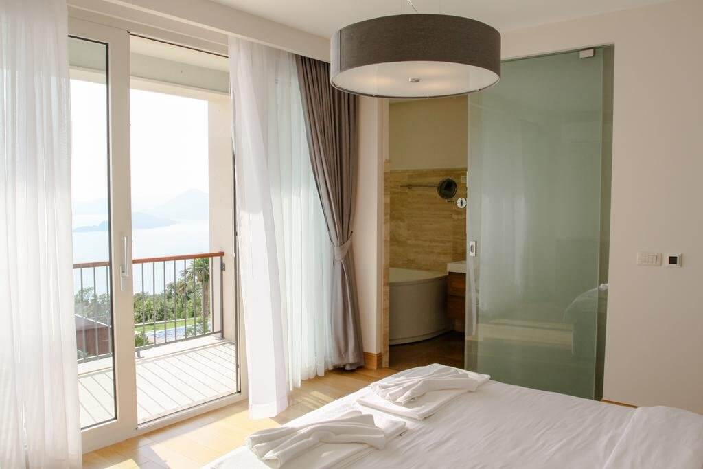 Spavaća soba u vili u Blizikućama, Crna Gora: panoramski pogled na more, balkon, staklena pregrada i kupatilo.