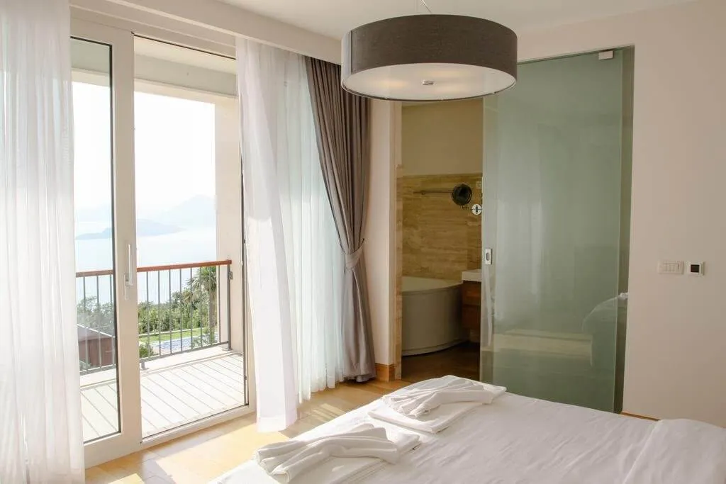 Sypialnia w willi w Blizikuće, Czarnogóra: panoramiczny widok na morze, balkon, szklana przegroda i łazienka.