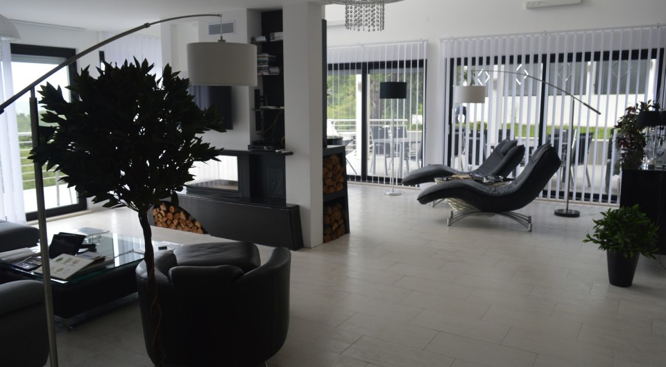 Karadağ, Tivat’taki villada modern oturma odası: deri mobilyalar, odunlu şömine ve teraslı panoramik pencereler.