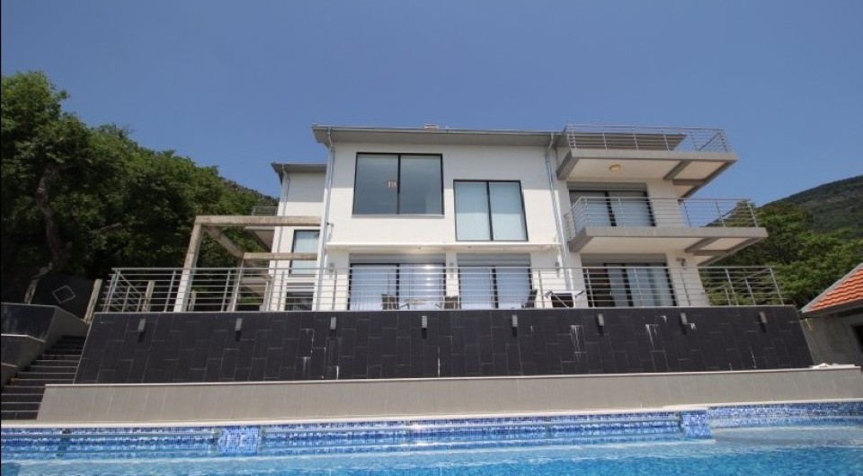 Karadağ, Tivat’ta havuzlu ve teraslı modern üç katlı villa: cephe ve bahçe alanı görünümü.