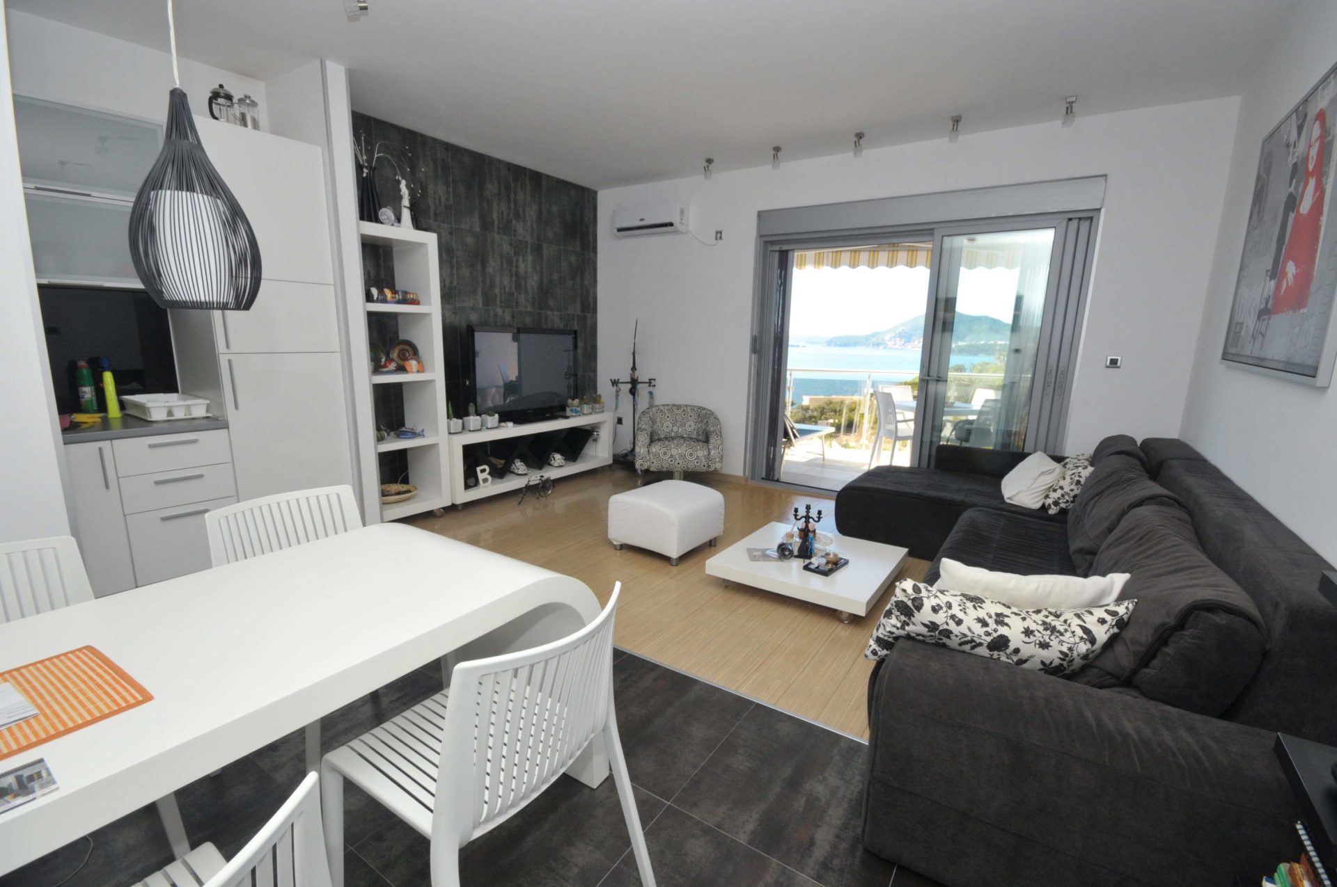 Modernes Wohnzimmer mit Meerblick in einer Wohnung in Pržno, Montenegro: weiße Möbel, dunkles Sofa und Zugang zur Terrasse.