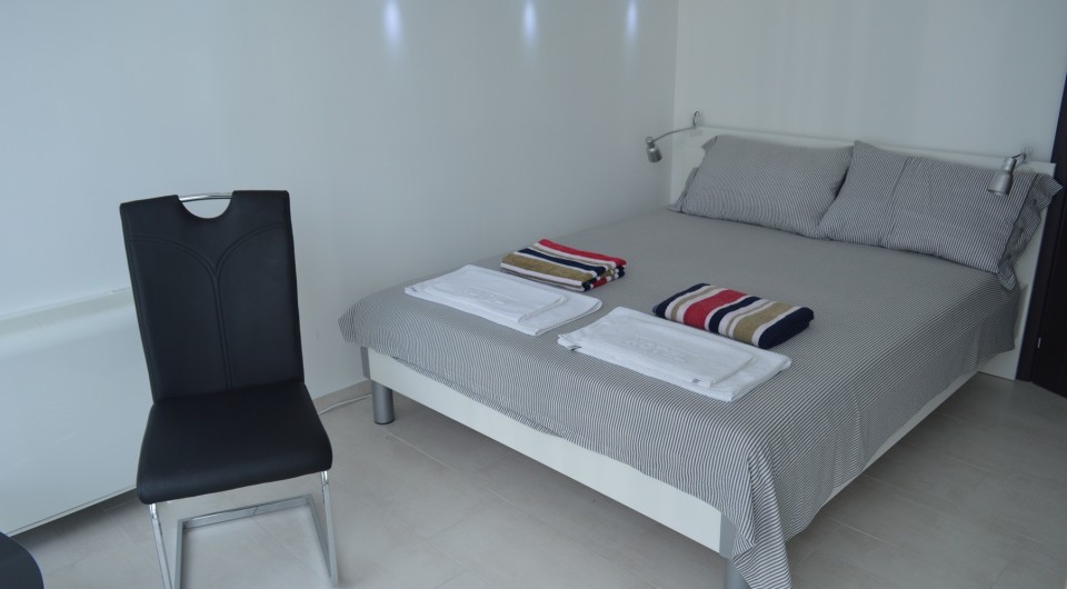 Tivat, Karadağ’daki villada çift kişilik yatak ve siyah sandalye bulunan aydınlık yatak odası. Modern iç mekan.