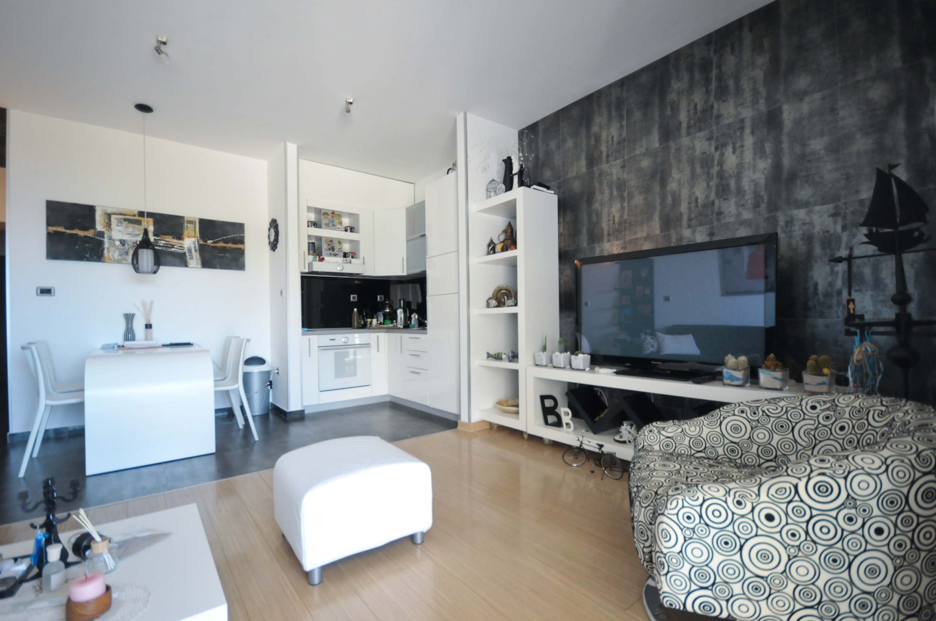Modernes Wohnzimmer mit Küche in einer Wohnung in Pržno, Montenegro: weiße Möbel, Akzentwand und Essbereich.