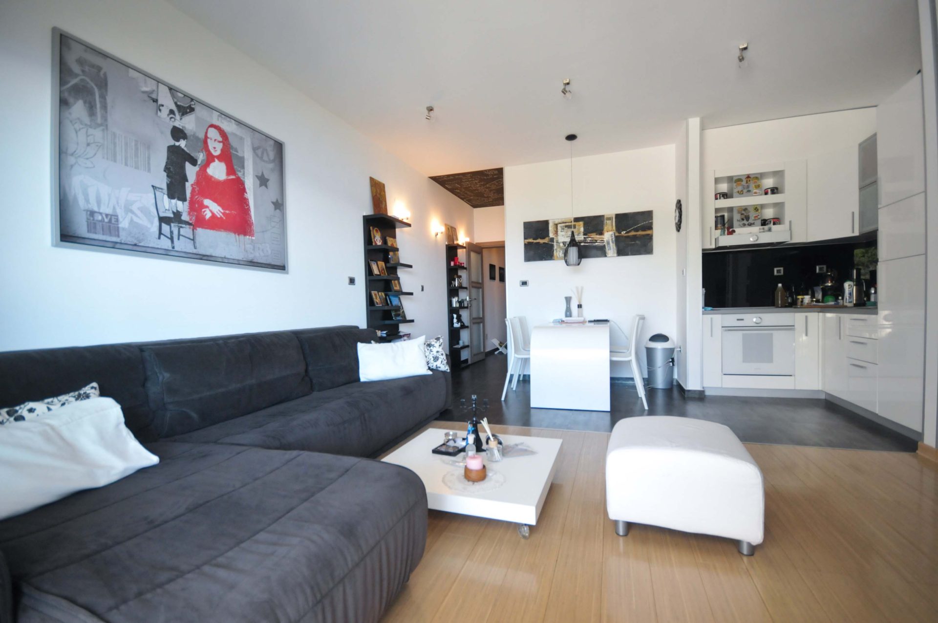 Modernes Wohnzimmer mit Küche in einer Wohnung, Pržno, Montenegro: graues Sofa, weiße Möbel und stilvolle Wanddekoration.