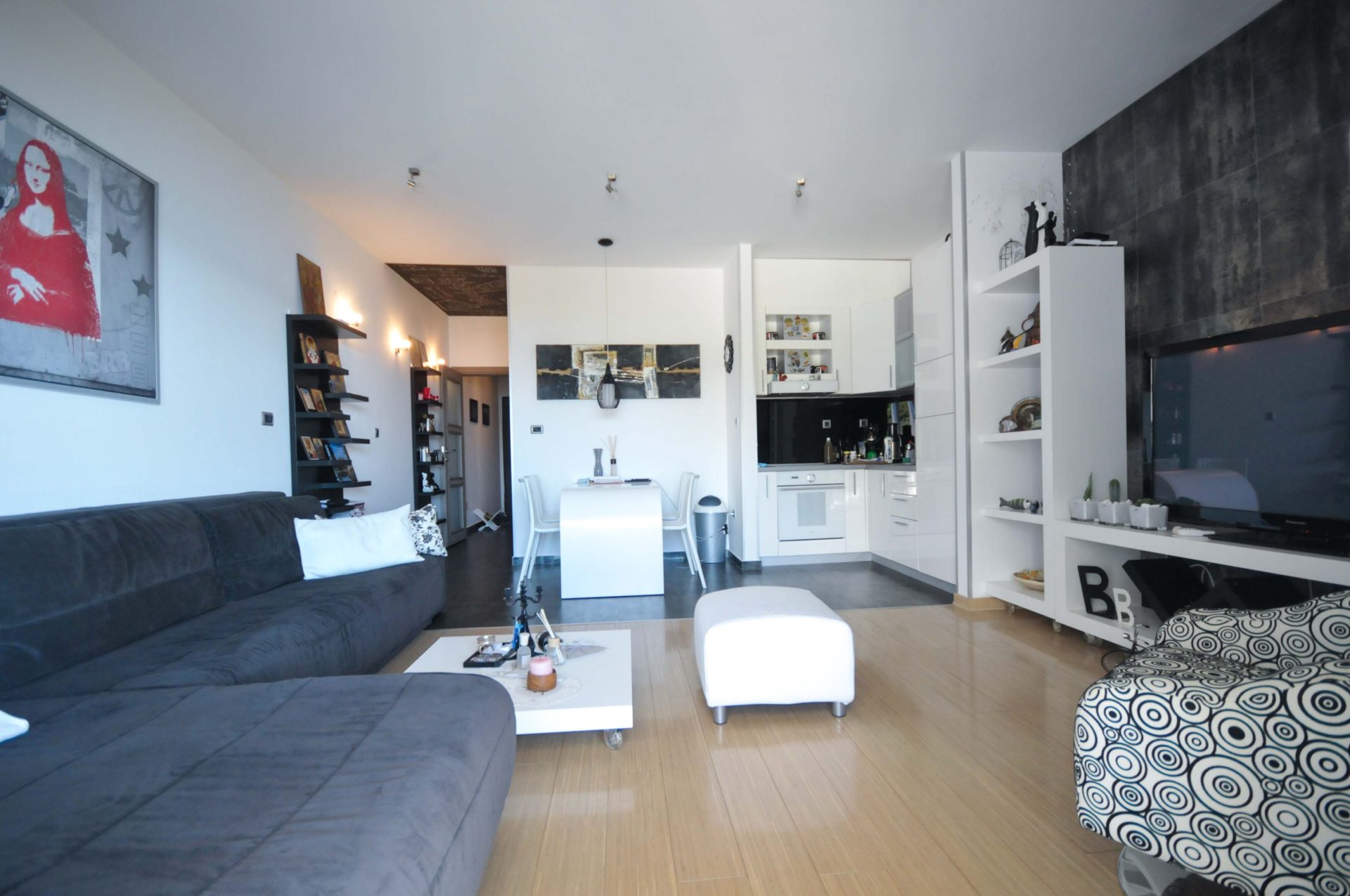 Modernes Wohnzimmer mit Küche in einer Wohnung in Pržno, Montenegro: graues Sofa, weiße Möbel und stilvolles Interieur.