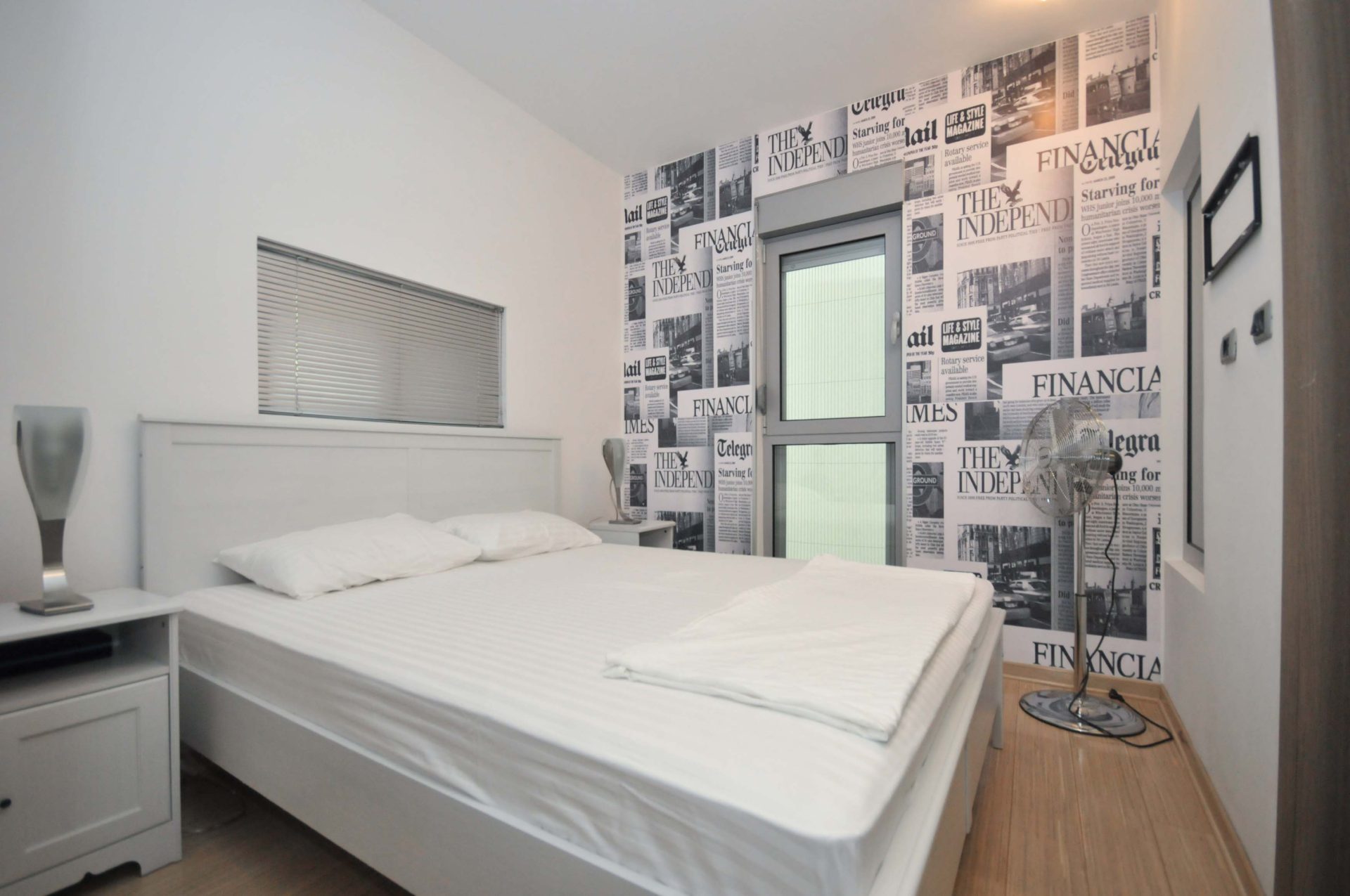 Schlafzimmer mit Doppelbett und Tapete im Zeitungsdruck-Stil in einer Wohnung in Pržno, Montenegro.