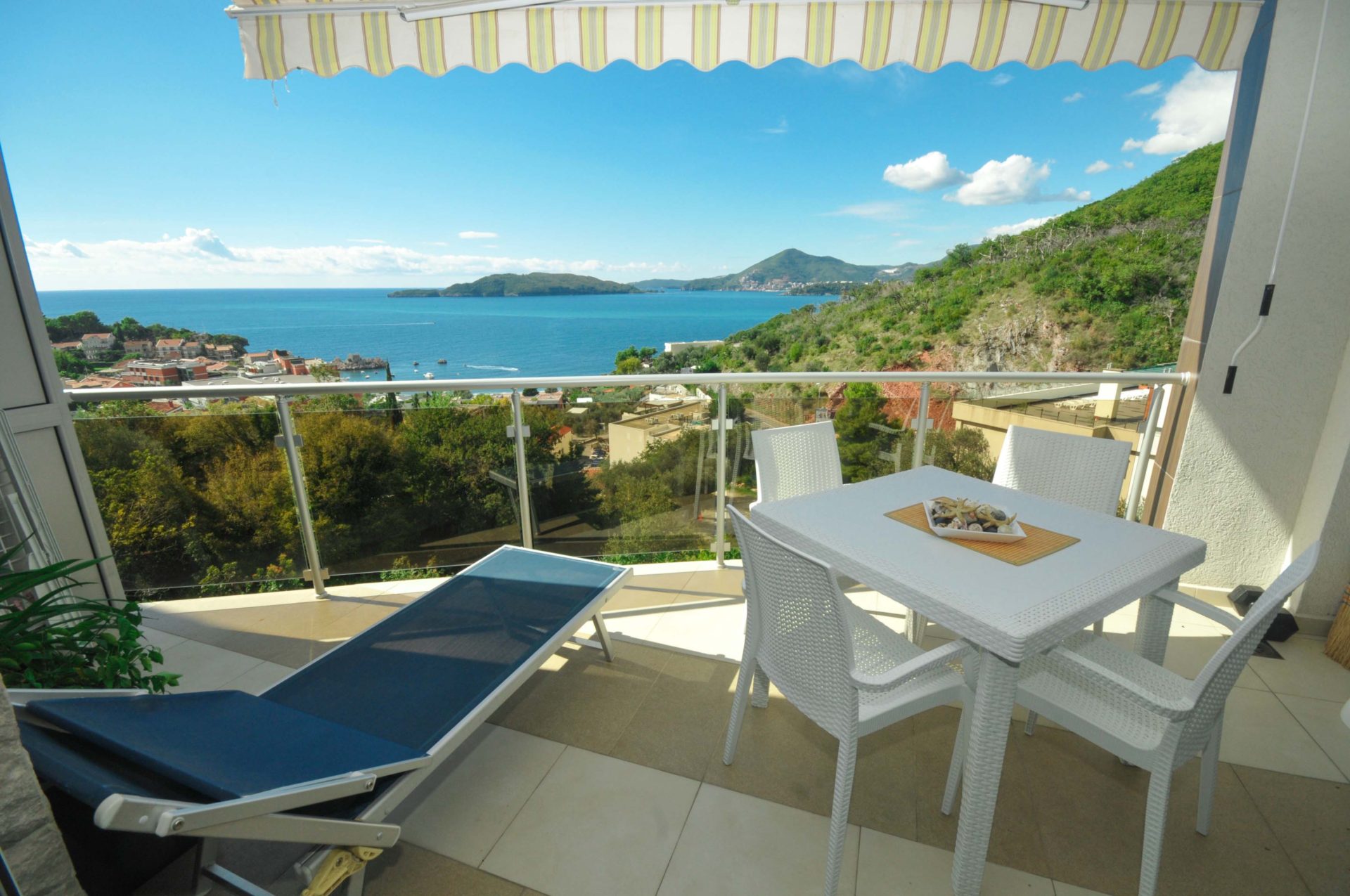 Terrasse mit Möbeln und Panoramablick auf das Meer in einer Wohnung in Pržno, Montenegro: Liegestuhl, Esstisch und Überdachung.