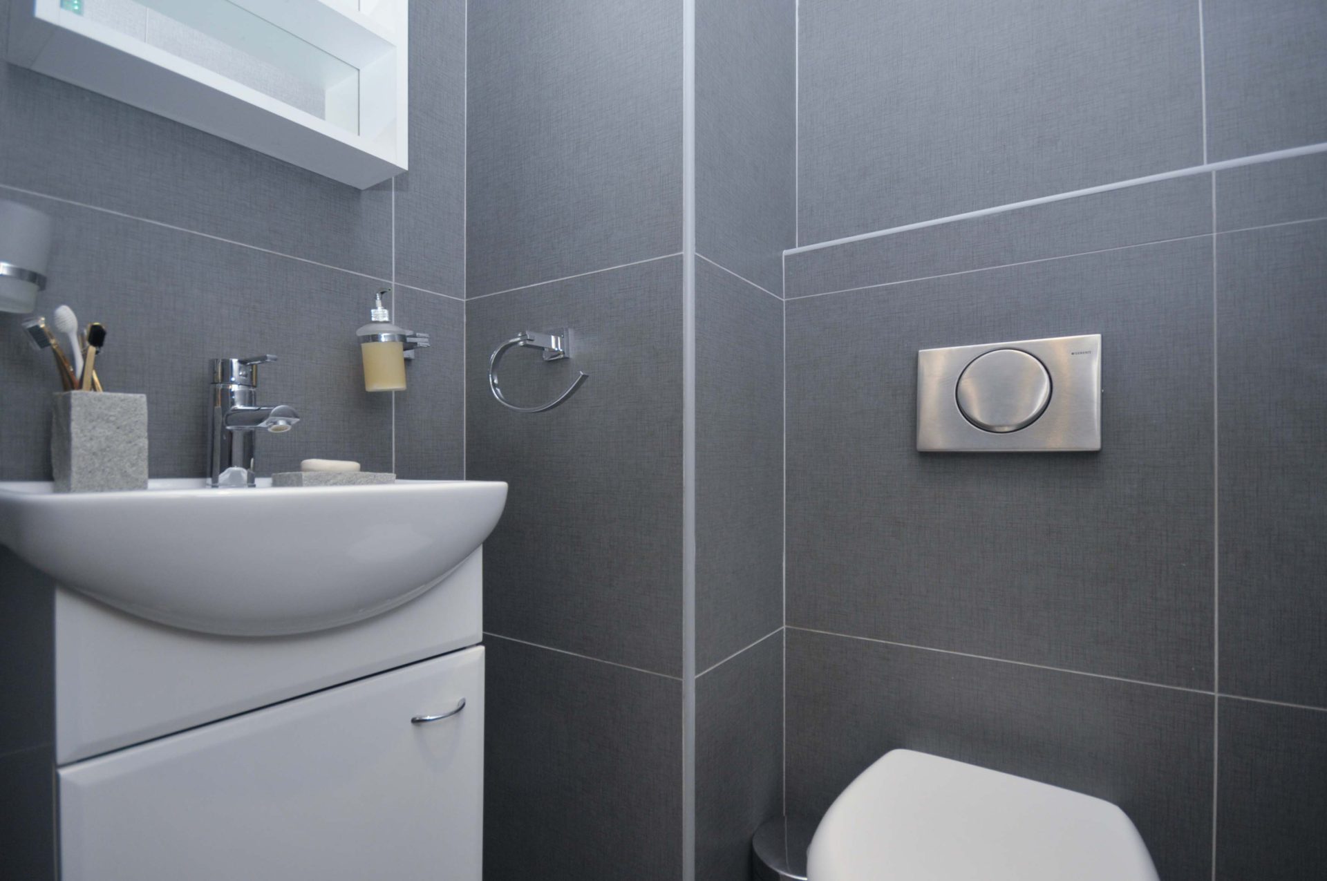 Modernes Badezimmer mit grauen Fliesen und weißer Sanitärkeramik in einer Wohnung in Pržno, Montenegro.
