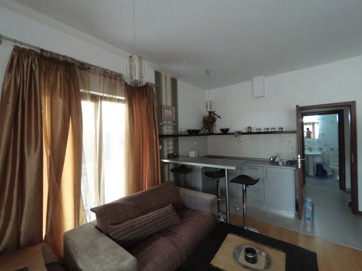 Wohnzimmer mit Küche und Bartheke in einer Wohnung in Budva, Montenegro: moderne Möbel, helle Ausstattung und Zugang zum Balkon.