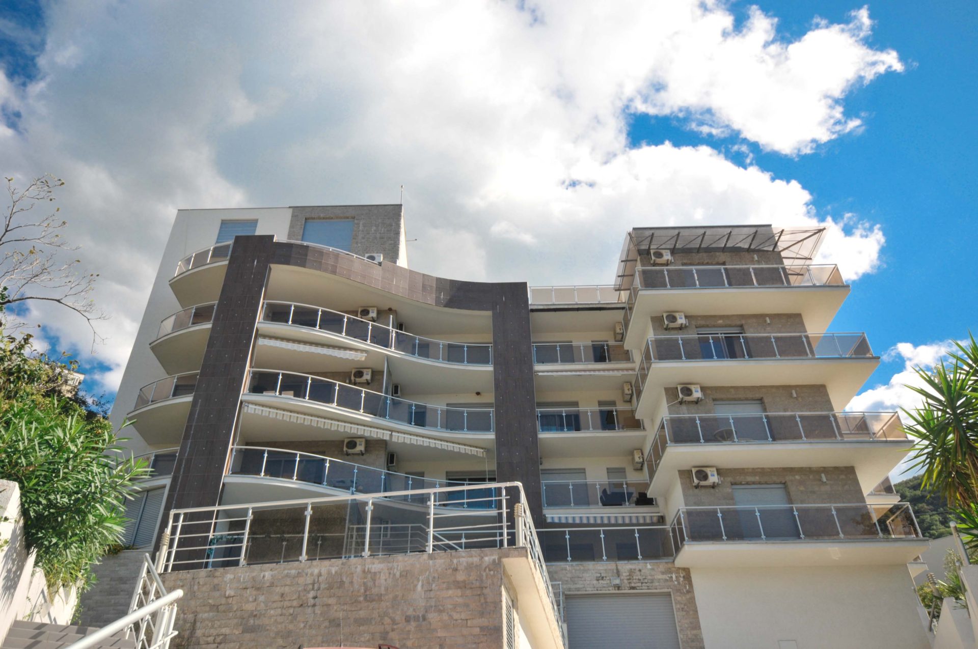Modernes Mehrfamilienhaus mit Terrassen in Pržno, Montenegro: Fassade mit Panoramabalkonen und Steinverkleidung.