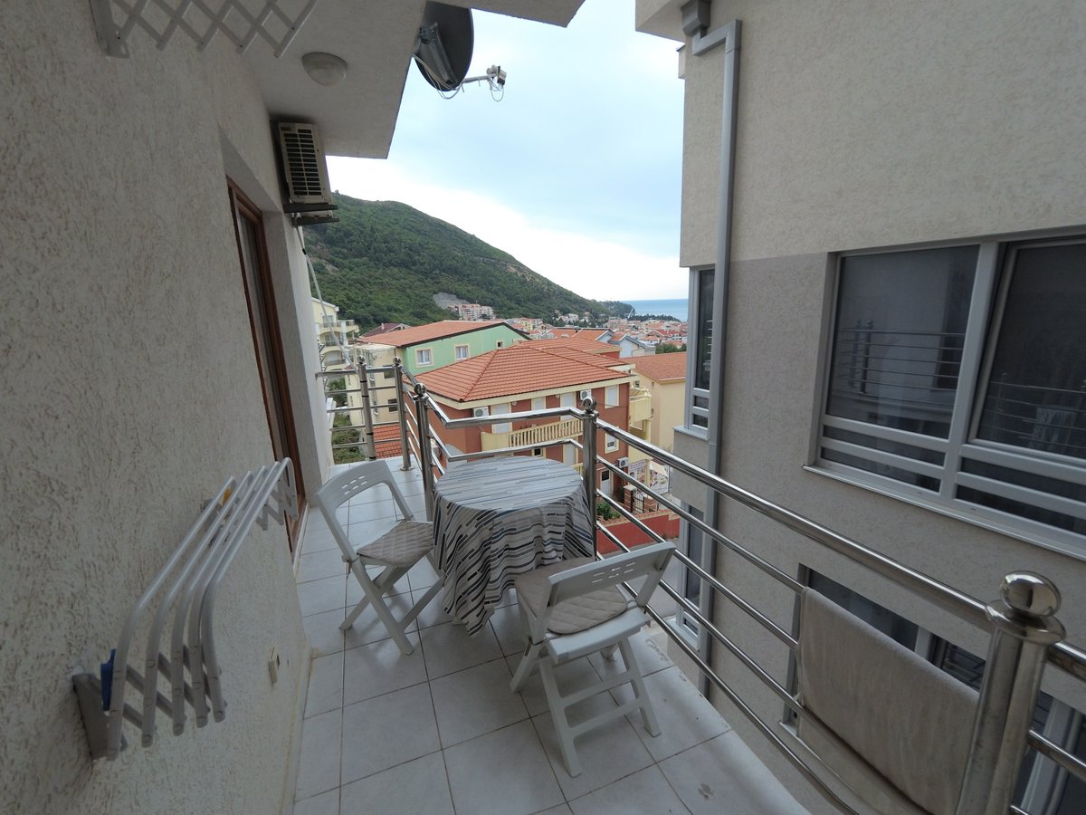 Balkon sa nameštajem i pogledom na planine i more u stanu u Budvi, Crna Gora: stočić, stolice i obloga od pločica.