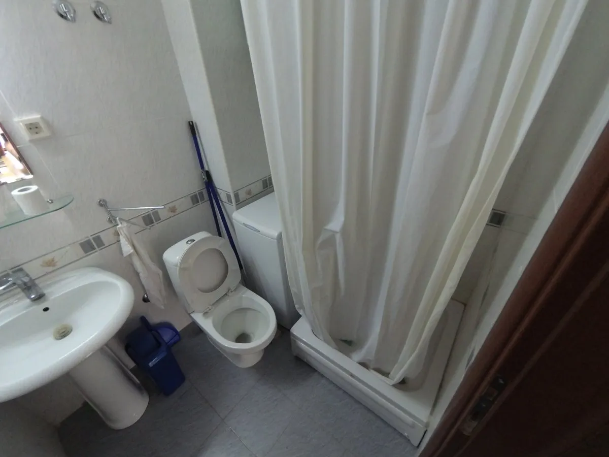 Badezimmer in einer Wohnung in Budva, Montenegro: helle Fliesen, Sanitäranlagen, Duschkabine und Waschmaschine.