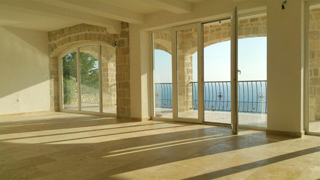 Karadağ, Drobni Pijesak’taki villada aydınlık oturma odası: taş kemerler, panoramik pencereler ve deniz manzaralı teras.