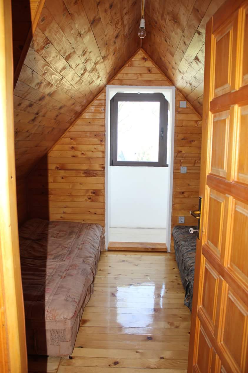 Chambre mansardée dans une maison à Sutomore, Monténégro : revêtement mural en bois, deux lits et accès au balcon.