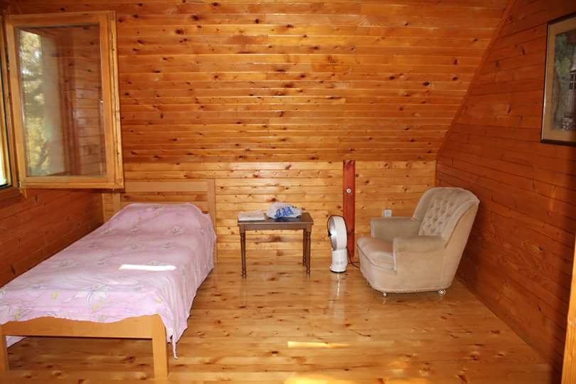 Chambre à coucher dans une maison en bois à Sutomore, Monténégro : lit simple, fauteuil et finition en lambris sous les combles.