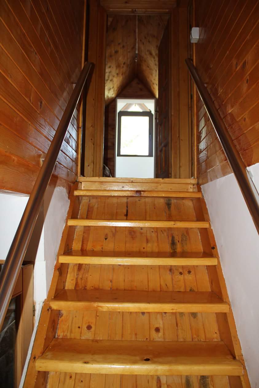 Escalier en bois dans une maison à Sutomore, Monténégro : finition en bois naturel et vue sur l’ouverture lumineuse vers le grenier.