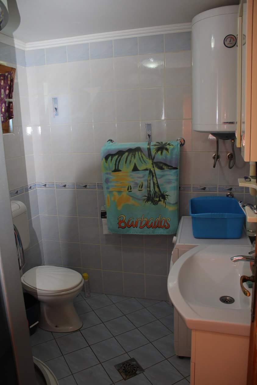 Salle de bains dans une maison à Sutomore, Monténégro : carrelage clair, sanitaires, chauffe-eau et machine à laver dans l’intérieur.
