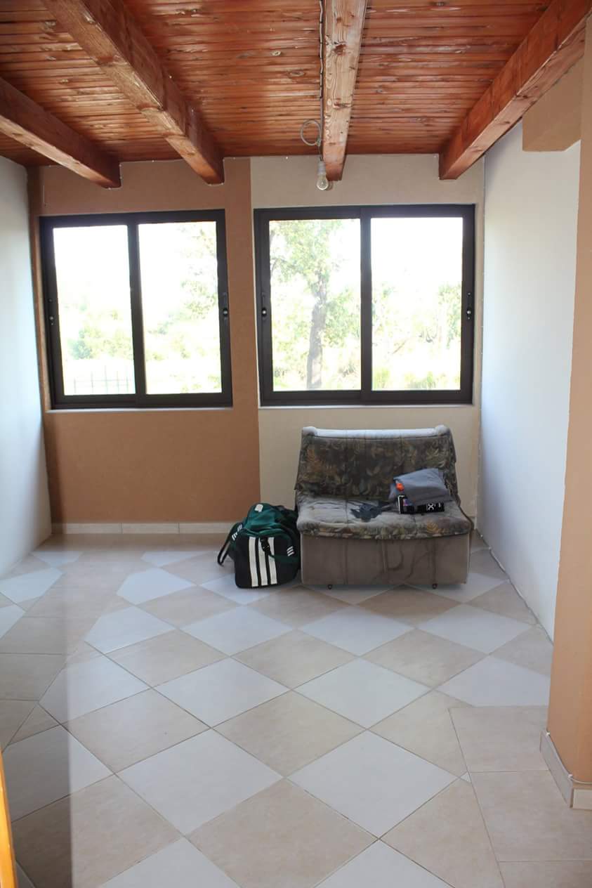 Salon dans une maison à Sutomore, Monténégro : pièce lumineuse avec plafond en bois, carrelage au sol et vue sur le jardin.