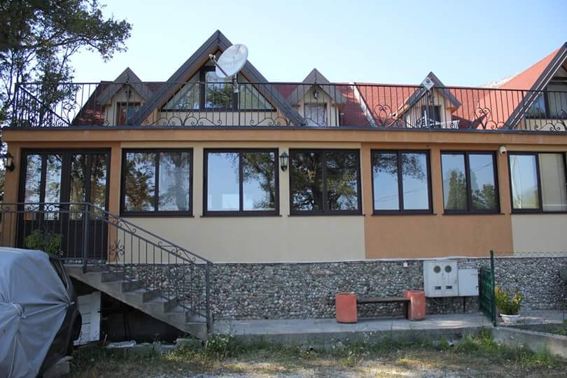 Maison à deux étages à Sutomore, Monténégro : façade avec revêtement en pierre, fenêtres panoramiques et terrasse avec garde-corps en fer forgé.