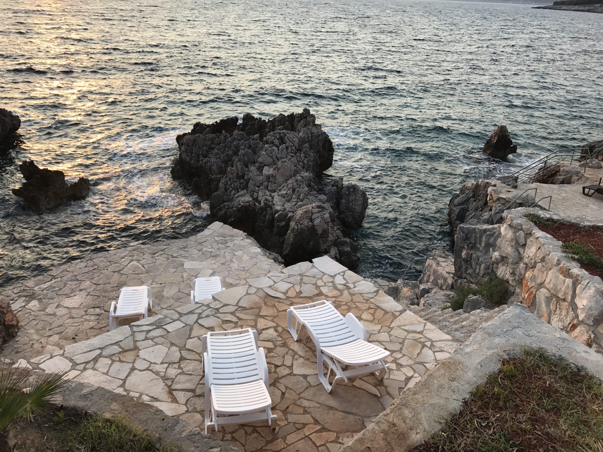 Terrasse mit Liegestühlen am Meer in einer Villa in Utjeha, Montenegro: Steinterrasse, felsige Küste und Blick auf die Adria.