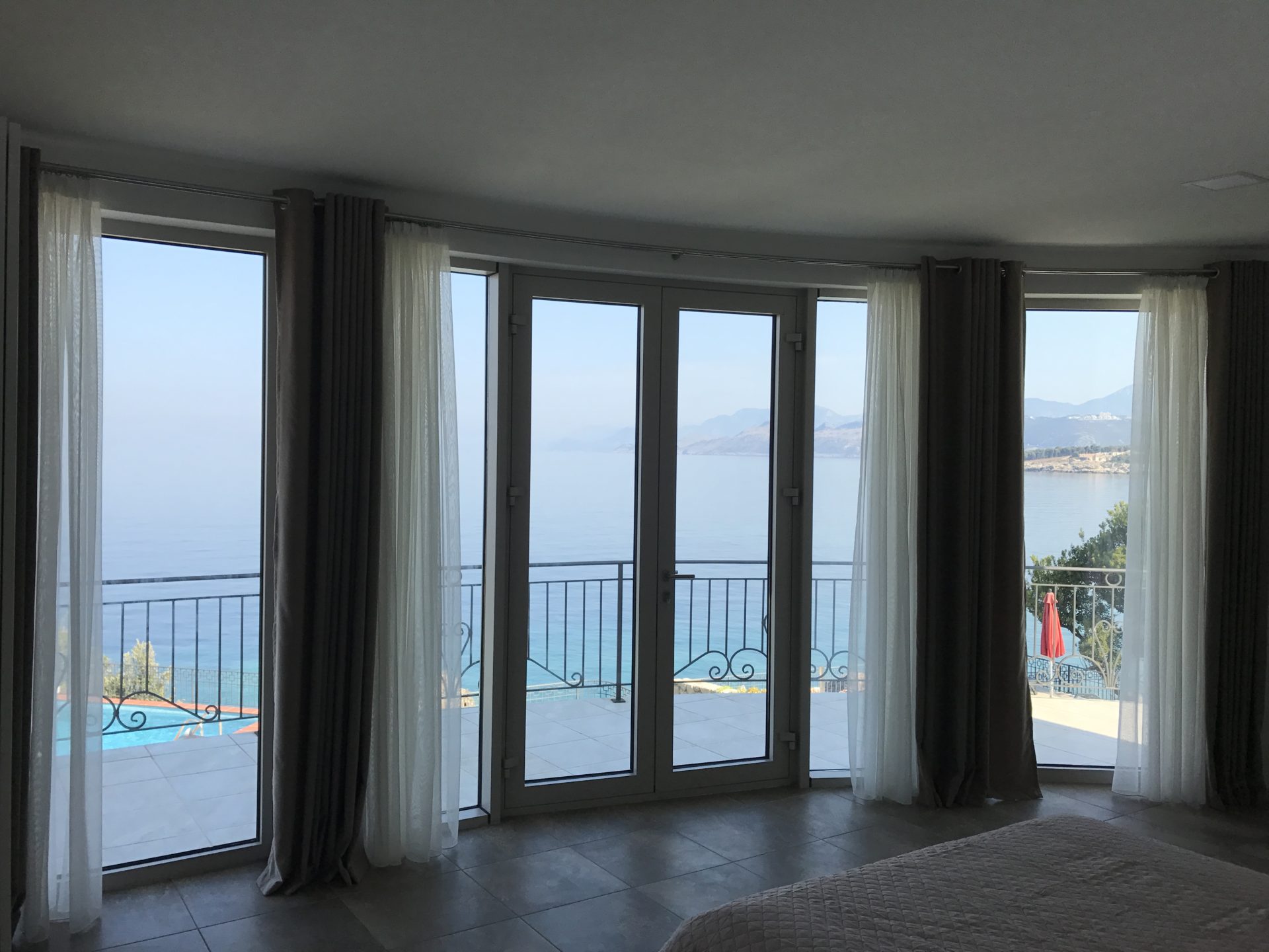Schlafzimmer mit Panoramablick auf das Meer und den Pool in einer Villa in Uteha, Montenegro: Glastüren und Terrasse.