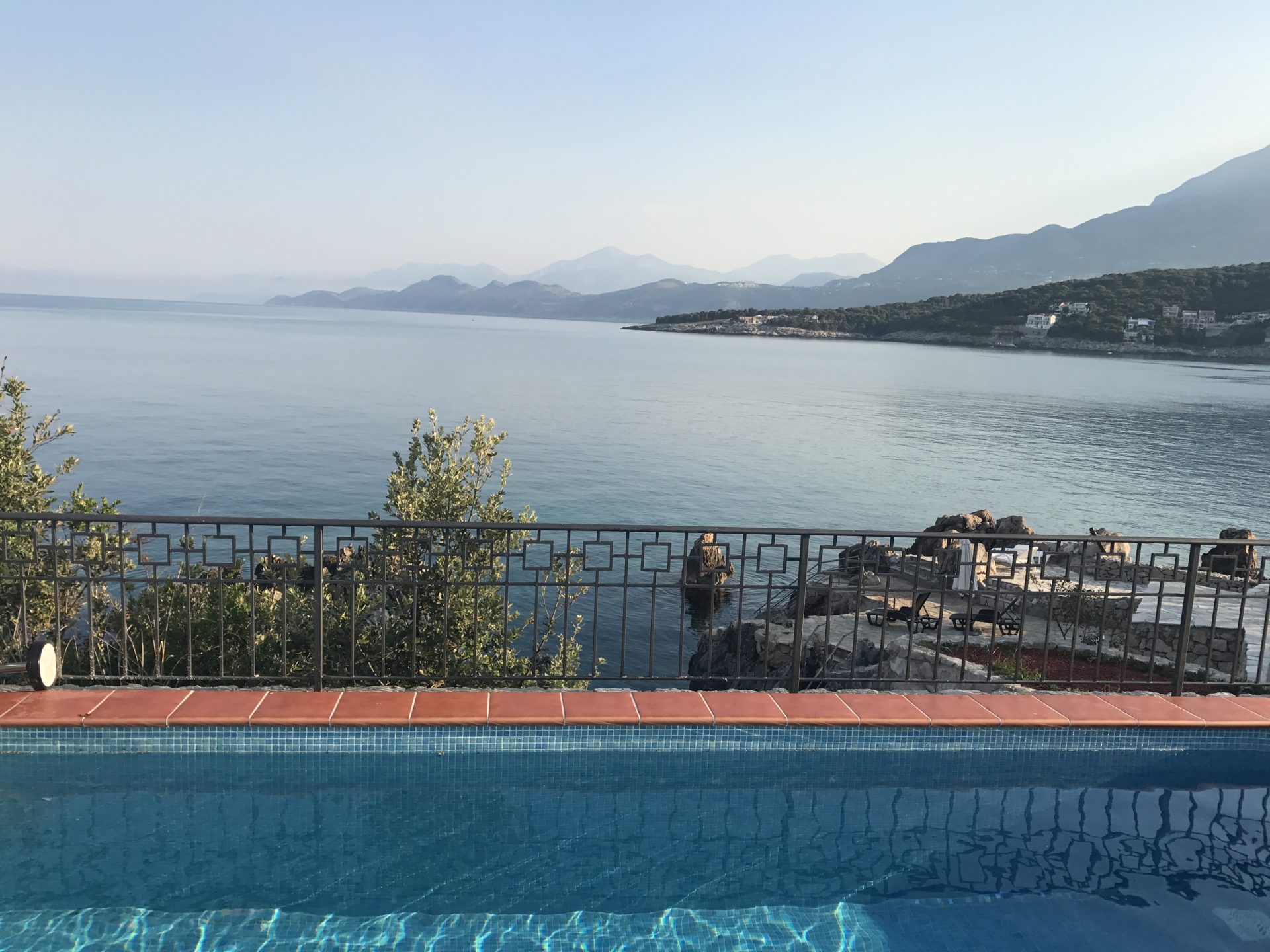 Blick auf das Meer und die Berge vom Pool der Villa in Utjeha, Montenegro: Panoramaterrasse mit Geländer und Ruhebereich am Wasser.