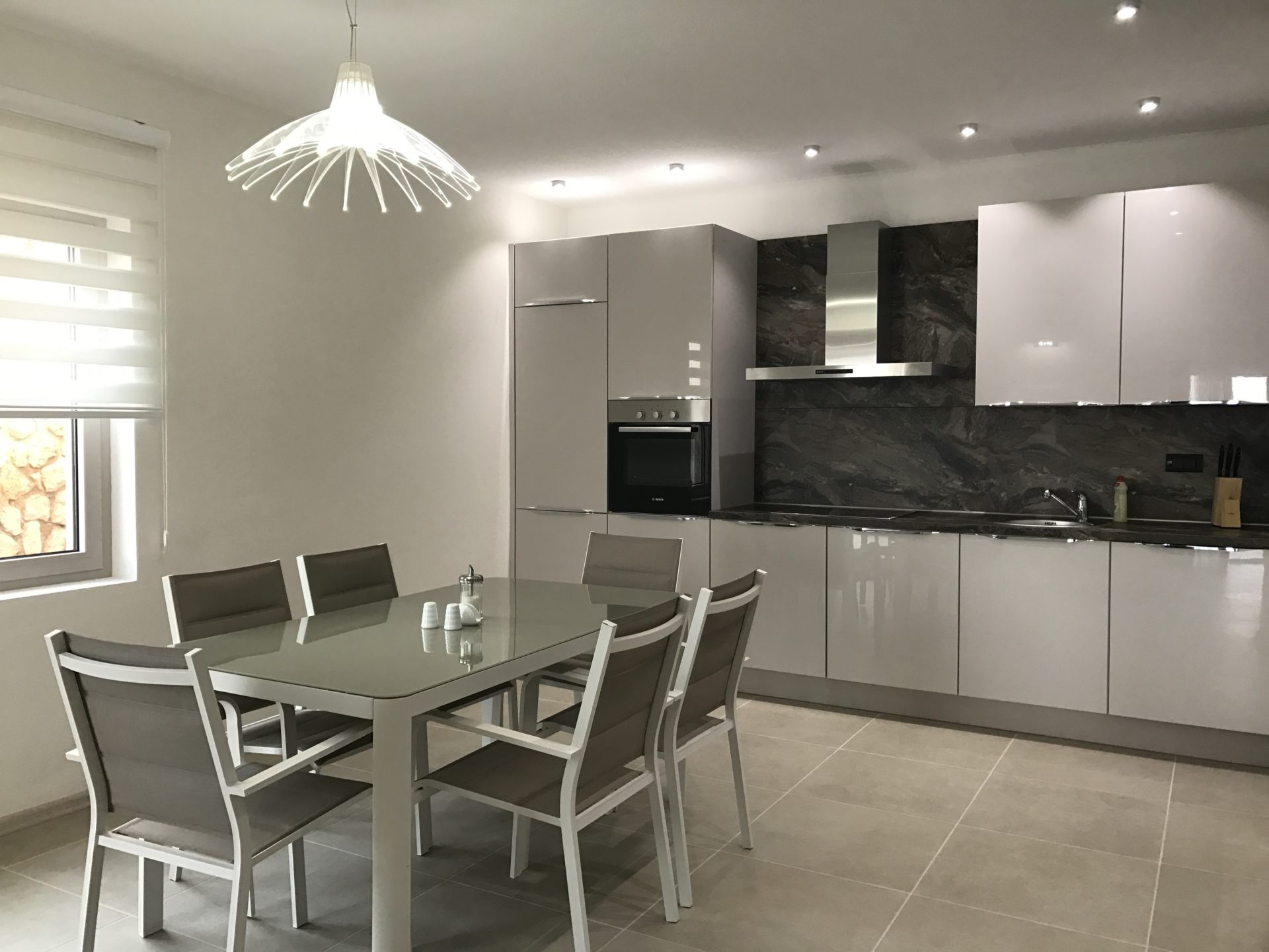 Moderne Küche mit Essbereich in einer Villa in Utjeha, Montenegro: glänzende Küchenzeile, Einbaugeräte und Essgruppe.