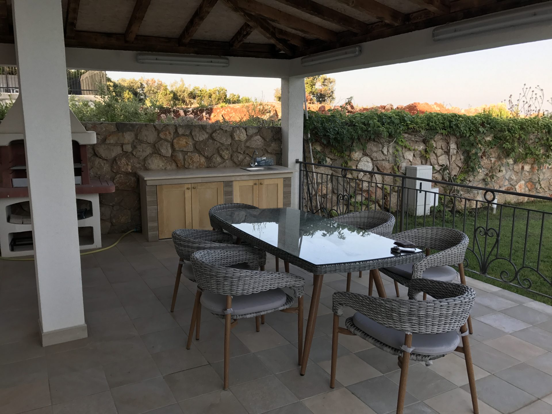 Überdachte Terrasse mit Grill und Essbereich in einer Villa in Utjeha, Montenegro: Rattanmöbel und Steinverkleidung.