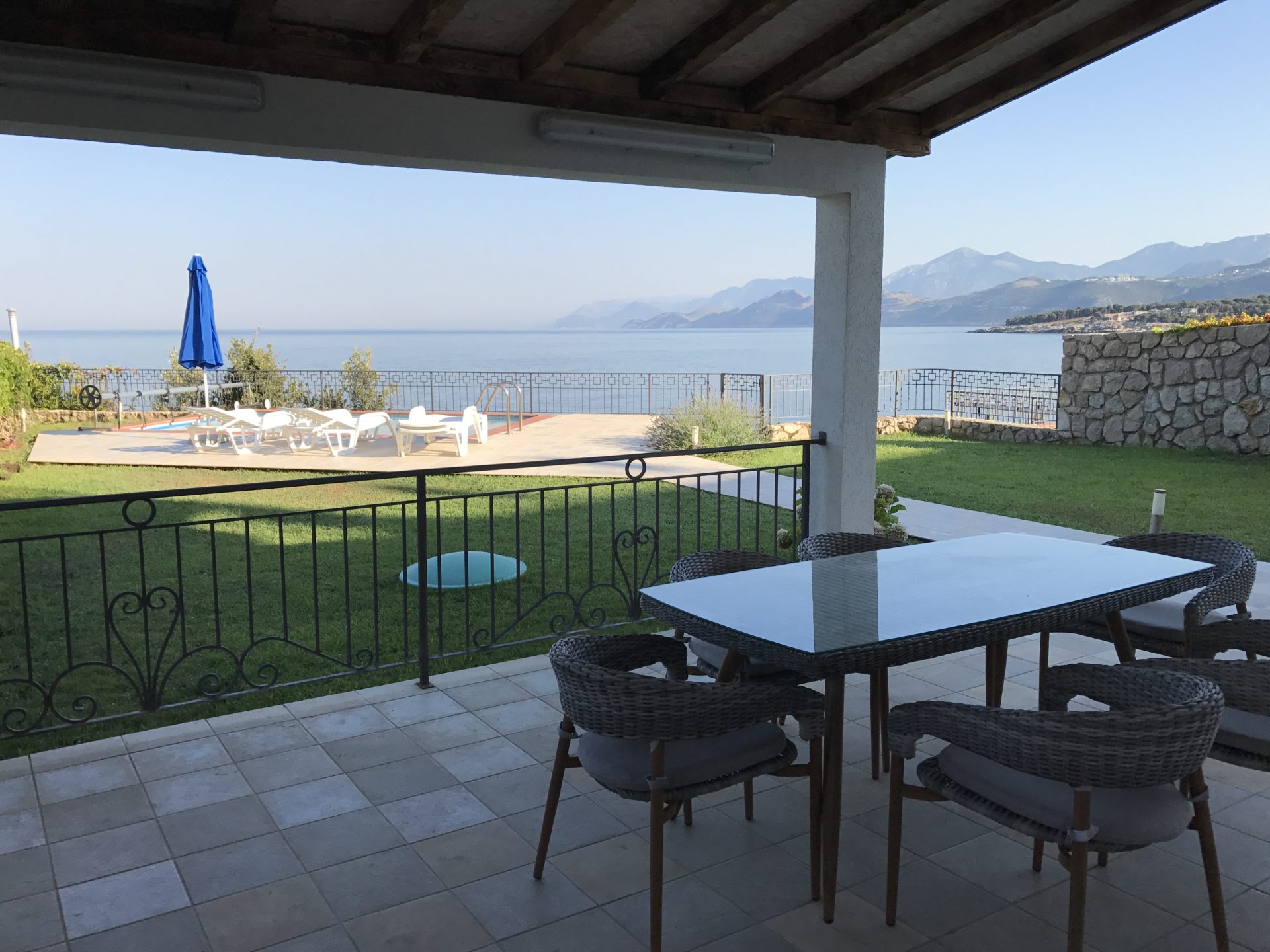 Terrasse der Villa in Utjeha, Montenegro: Rattanmöbel, Meerblick, Pool und Berge, Fliesenbelag und Rasen.