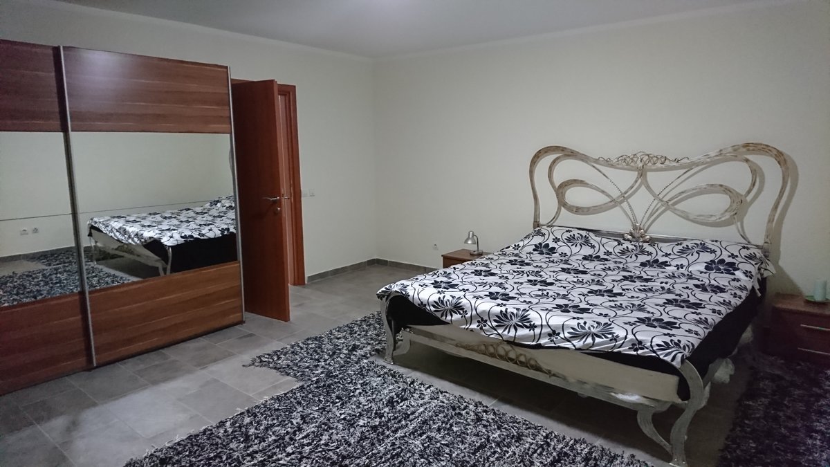Schlafzimmer in einer Villa in Uteha, Montenegro: Doppelbett mit schmiedeeisernem Kopfteil, Kleiderschrank mit Spiegeltüren und Fliesenboden.