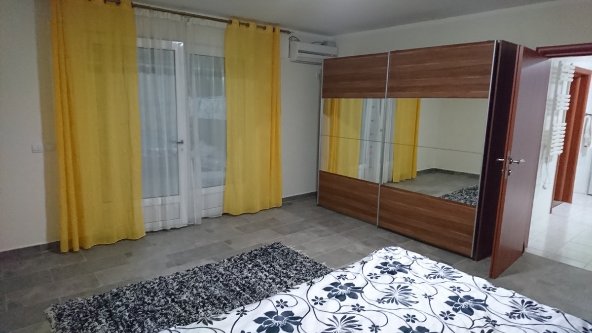 Schlafzimmer in einer Villa in Utjeha, Montenegro: Doppelbett, Kleiderschrank mit Spiegeltüren, gelbe Vorhänge und Zugang zur Terrasse.