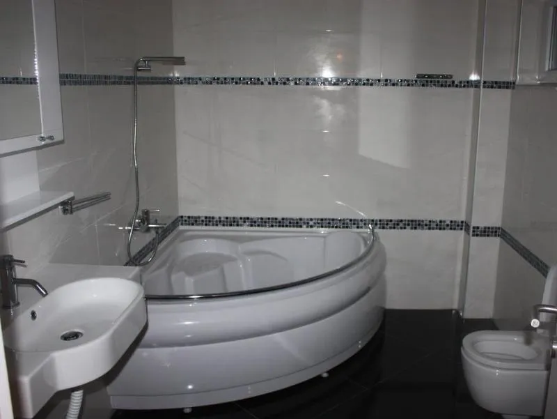 Savremeno kupatilo u kući u Tivtu, Crna Gora: ugaona kada, svetle pločice i sanitarije u enterijeru.