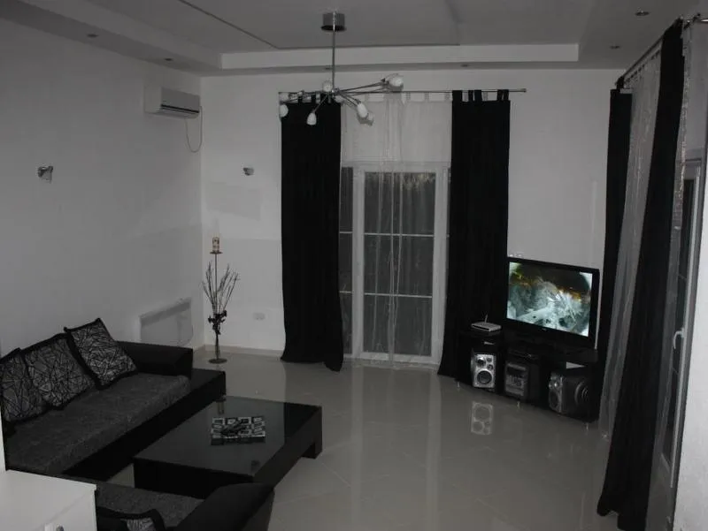 Savremeni dnevni boravak u kući u Tivtu, Crna Gora: siva sofa, sjajan pod, crne zavese i TV zona.
