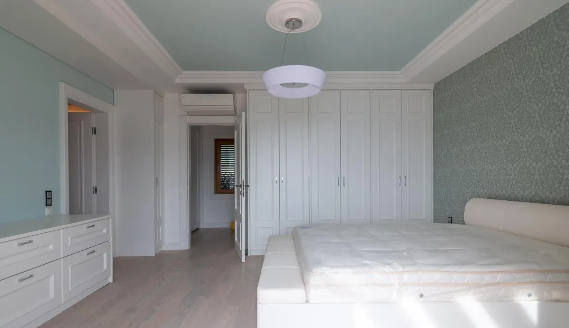Une chambre lumineuse avec une armoire blanche, un lit et une commode.