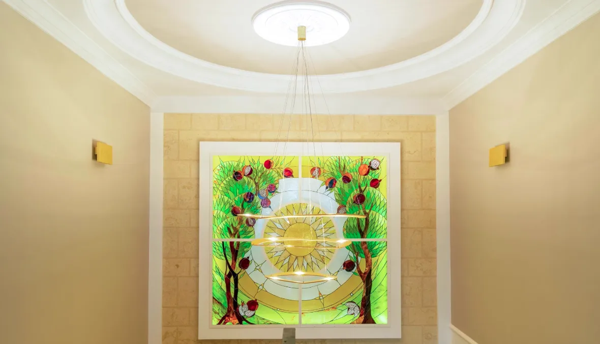 Vitrail avec des arbres et des fruits, lustre éclairé, murs jaunes