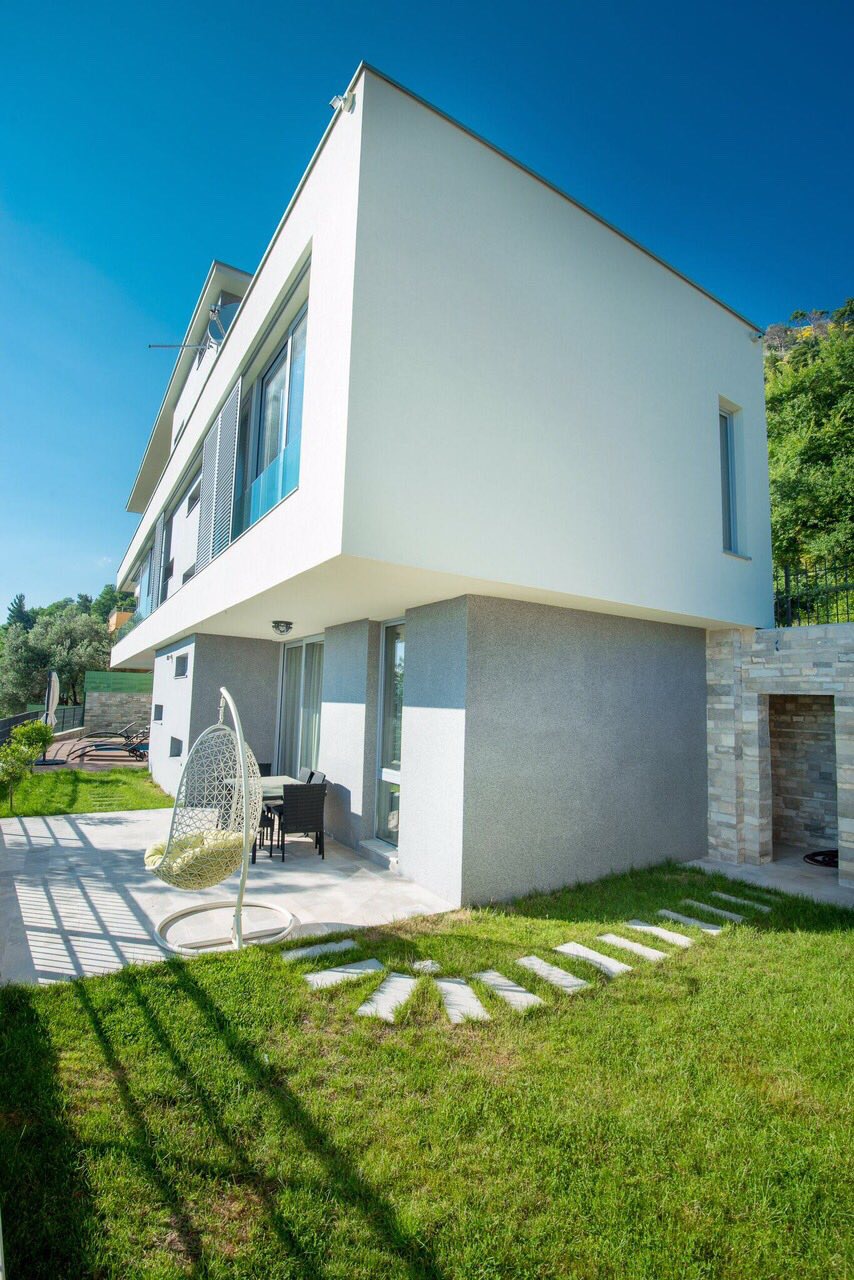 Karadağ, Kotor’da modern villa: asma sandalye, bahçe ve panoramik pencereli binanın cephesinin görüldüğü teras manzarası.
