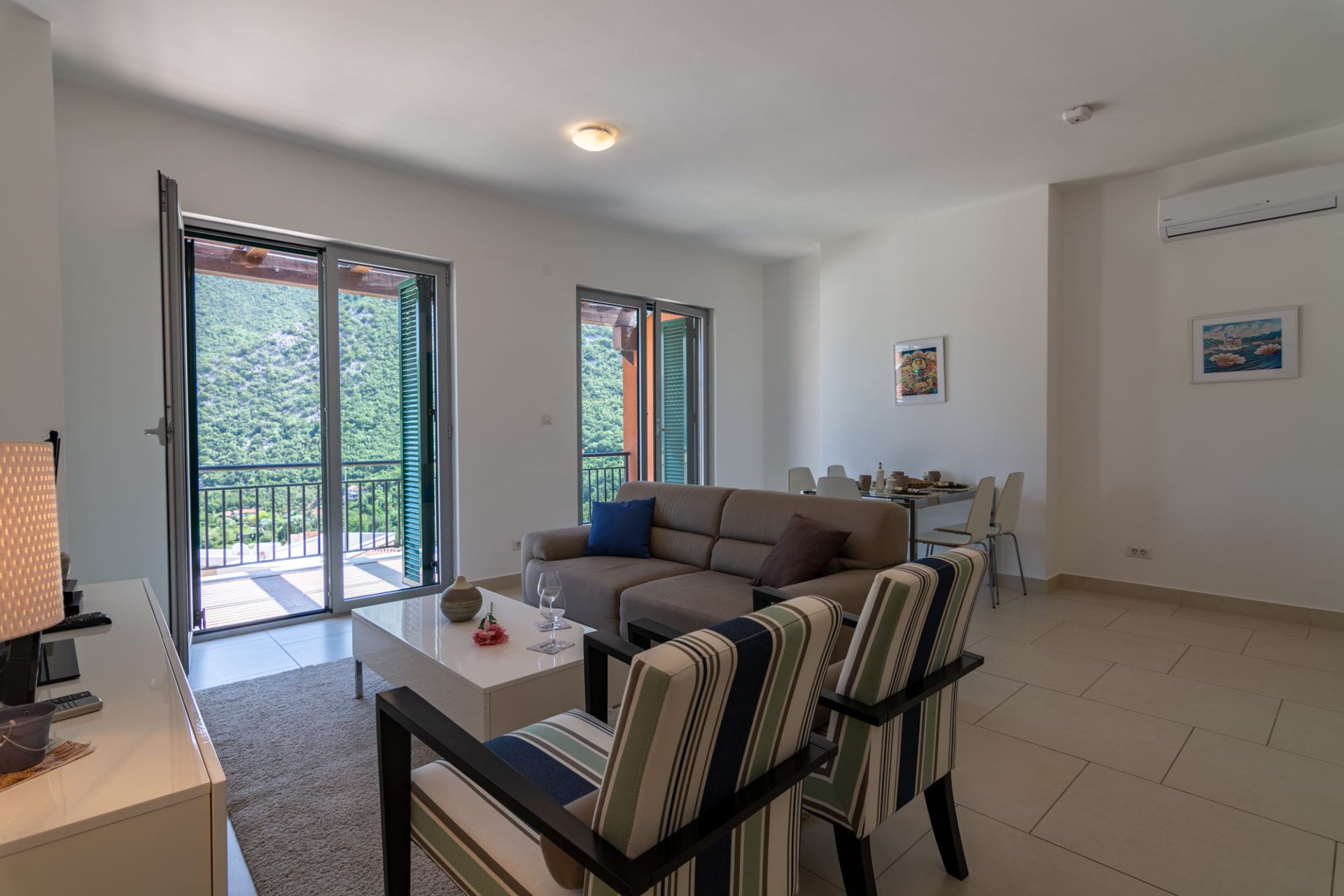 Salon w apartamencie w Morini, Czarnogóra: jasne pomieszczenie z miękkimi meblami, jadalnią i widokiem na góry.