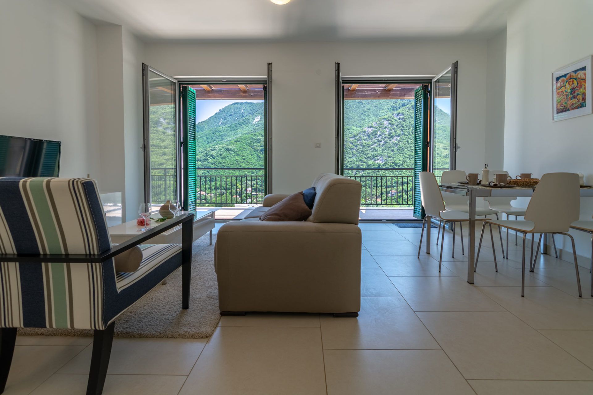 Salon w apartamencie w Morini, Czarnogóra: jasne wnętrze, miękkie meble i taras z widokiem na zielone góry.