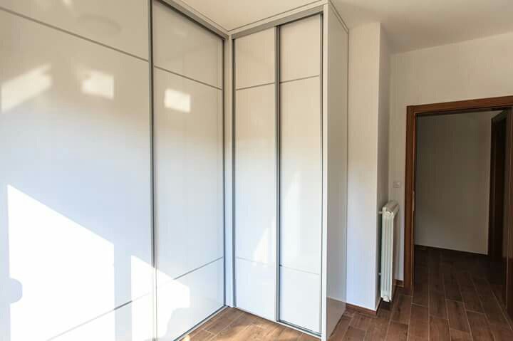 Ein eingebauter weißer Hochglanz-Schiebetürschrank im Schlafzimmer eines Hauses in Šušanj, Montenegro, mit Holzoptik-Bodenbelag.