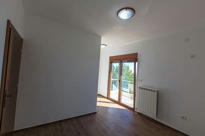 Helles Schlafzimmer mit Zugang zum Balkon im Haus, Shushan, Montenegro: Laminatboden, weiße Wände und Heizkörper.